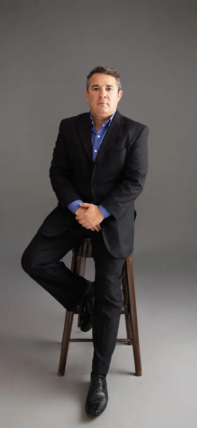 Advogado Vinicios Araujo de Souza, de terno escuro e camisa azul, sentado em uma banqueta alta